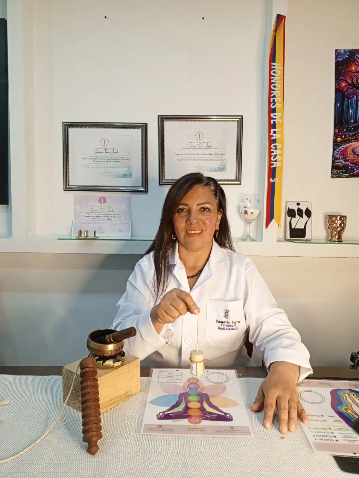 Damaris Torres en su consultorio, sosteniendo un péndulo sobre una tabla de chakras